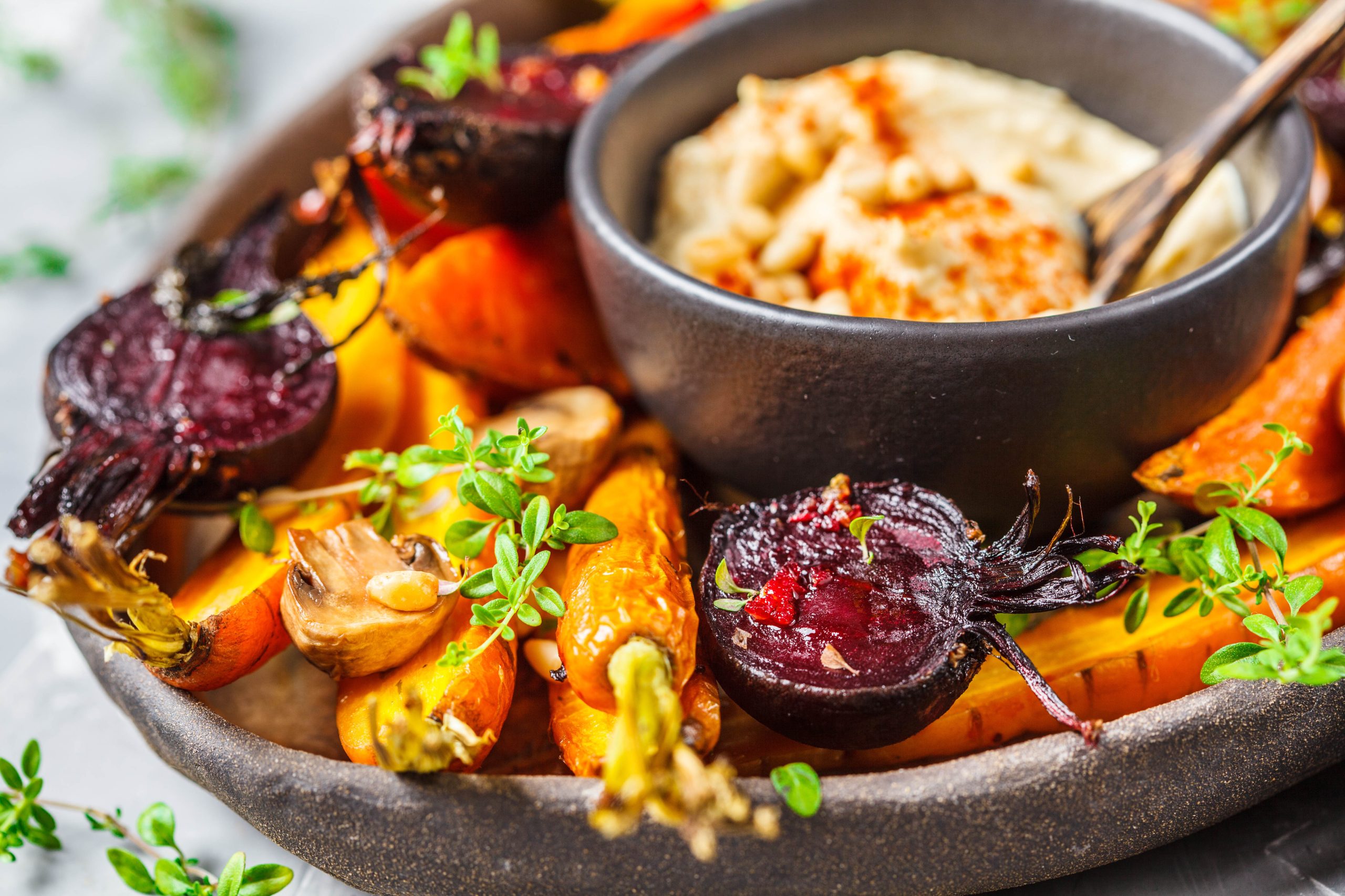 Baked carrots, beets, zucchini and yam with hummus in a dark dish.