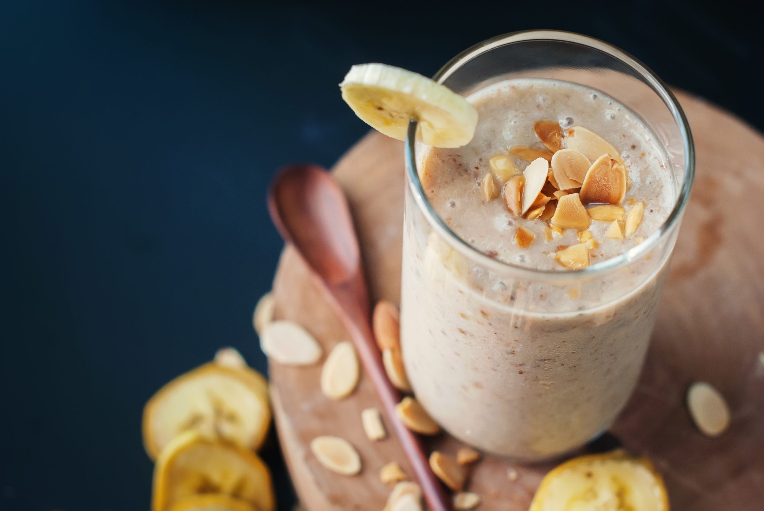 Fruit banana smoothies with milk, almond, flakes, and slices of banana on a black chalkboard